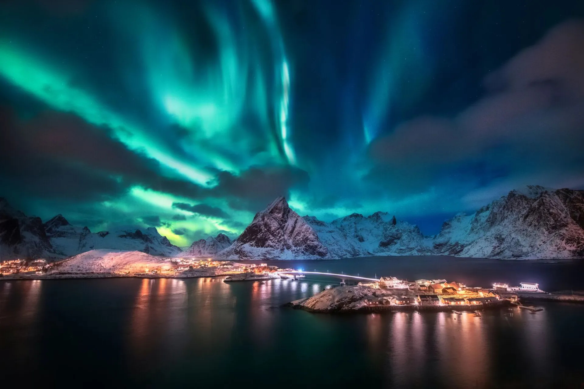 The Northern Lights over snow covered mountains by water in the Lofoten Islands, Norway